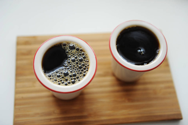 frischer schwarzer Filterkaffee in zwei Keramiktassen ohne Henkel auf Bambustablett. weißer Hintergrund. Ansicht von oben, Nahaufnahme - Foto, Bild