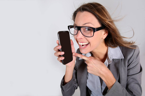 Business girl with funny look showing smartphone - Foto, imagen