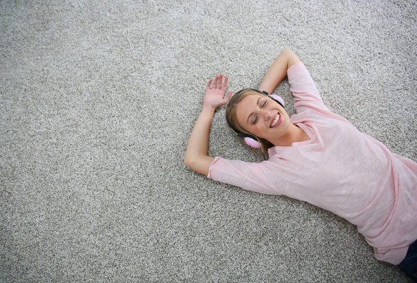 Blond girl relaxing on carpet floor with headphones on - Photo, Image