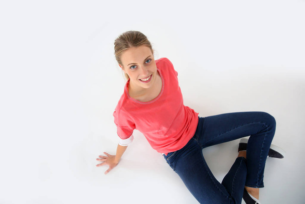 Blond woman with pink shirt sitting on floor, isolated - Foto, afbeelding