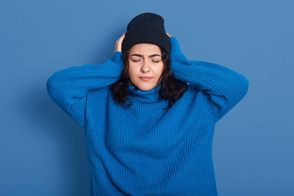 Close up portrait of unhappy woman touching head, unsatisfied female thinking about problem, feeling headache, suffering from pain, keeping eyes closed, posing isolated over blue studio background. - Foto, Bild