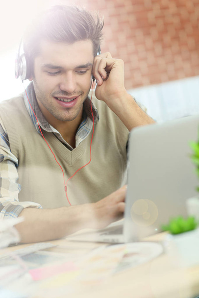 Young office worker using headphones in front of laptop - Foto, Imagen
