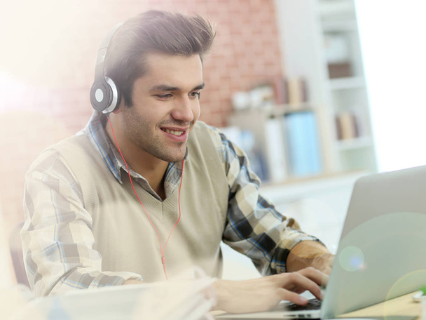 Young office worker using headphones in front of laptop - Foto, immagini