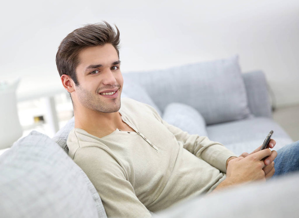 Smiling handsome man using smartphone sit in couch - Fotografie, Obrázek
