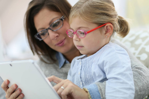 Mother and daughter with eyeglasses playing with tablet - Foto, imagen