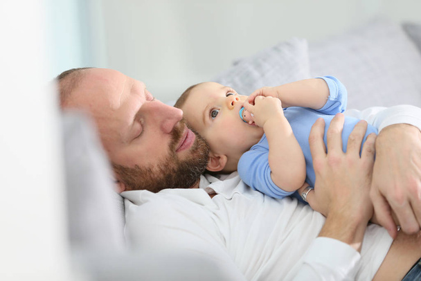Father with baby boy relaxing in sofa at home - Фото, зображення