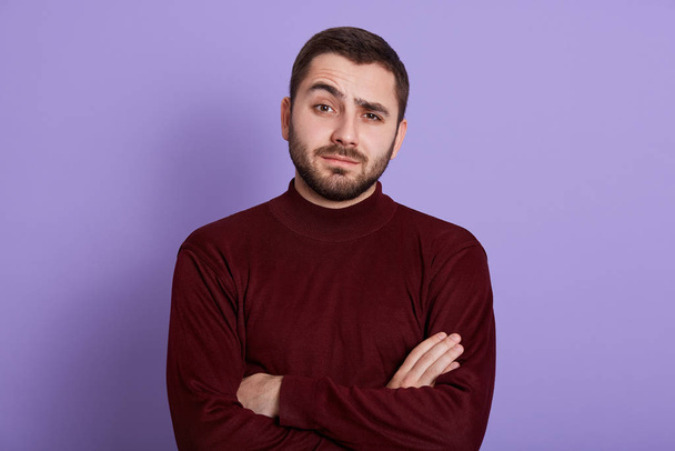 Indoor portrait of surprised impressed handsome man having folded arms, raising one eyebrow, having bewildered facial expression, looking directly at camera, being emotional. People concept. - Foto, imagen