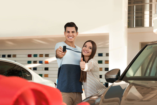 Happy couple with car key in modern auto dealership - Фото, изображение