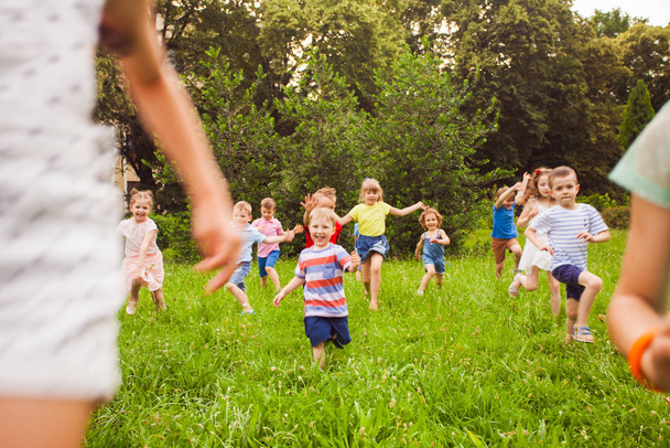 Grupo de niños de niños y niñas corren en parque sobre hierba verde
 - Foto, Imagen