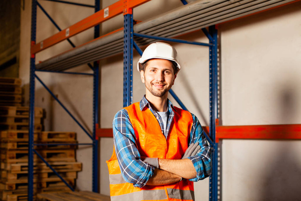 Confident handsome worker in protective hardhat and uniform at the warehouse of a industrial manufacturing - Photo, Image