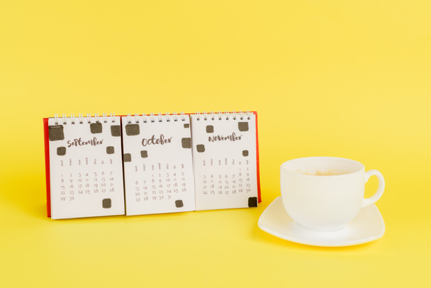 Calendar with autumn months and cup of coffee on yellow background - Photo, image