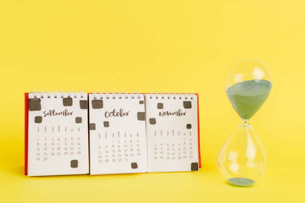 Hourglass near calendar with autumn mouths on yellow background - Photo, Image
