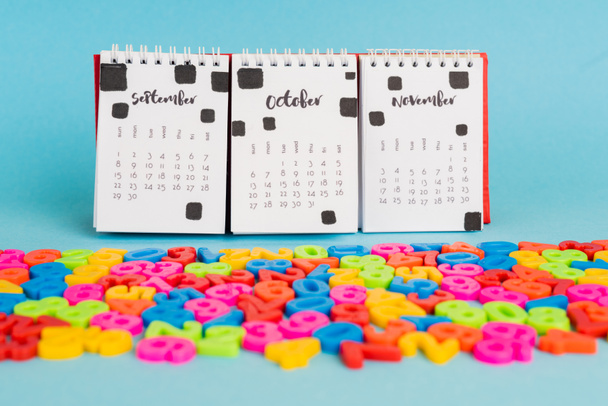 Kalender en kleurrijke plastic nummers op blauwe achtergrond - Foto, afbeelding