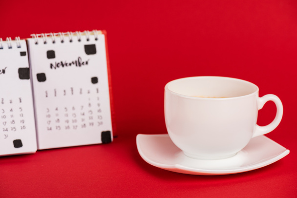 Selective focus of coffee cup and calendar on red background - 写真・画像