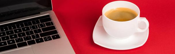 Panoraama laukaus kannettava tietokone tyhjä näyttö ja kahvikuppi punaisella pohjalla
 - Valokuva, kuva