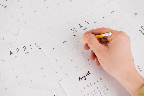 Cropped view of man holding pencil above monthly calendars  - Фото, изображение