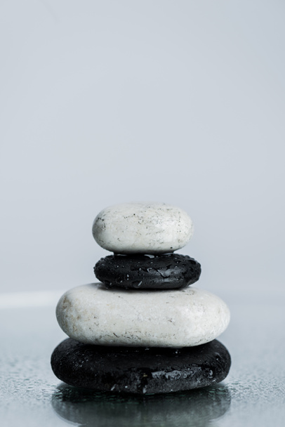 Piedras zen blancas y negras sobre vidrio húmedo aislado sobre gris
  - Foto, Imagen