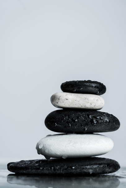 Vista de cerca de piedras zen apiladas en blanco y negro sobre vidrio húmedo aislado en gris
 - Foto, Imagen