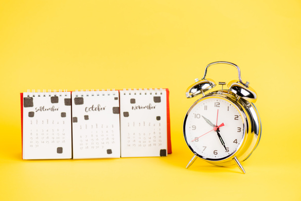 Sarı zemin üzerinde sonbahar ayları olan alarm saati ve takvimi - Fotoğraf, Görsel