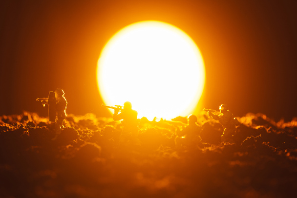 Escena de batalla de soldados de juguete con arma y puesta de sol en el fondo
 - Foto, Imagen