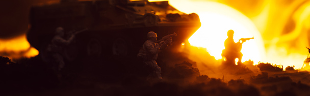 Kampfszene mit Spielzeugkriegern, Panzer und Feuer mit Sonnenuntergang im Hintergrund, Panoramaaufnahme - Foto, Bild
