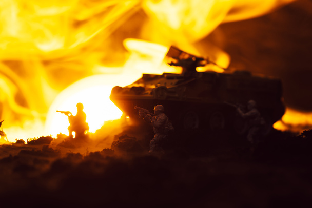 Солдаты-игрушки с танком, огнем и закатом на черном фоне, сцена боя
 - Фото, изображение