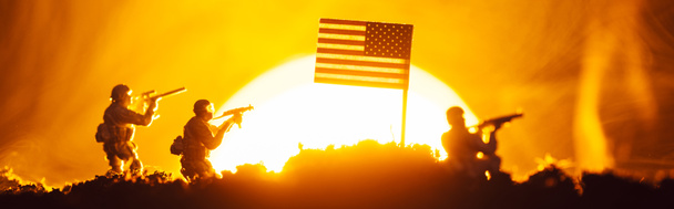 Сцена боя с игрушечными воинами возле американского флага в дыму с закатом на заднем плане, панорамный снимок
 - Фото, изображение