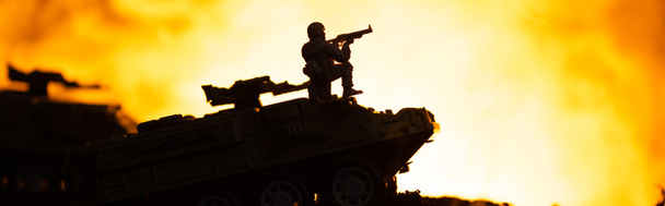 Battle scene with silhouette of toy soldier on tank with fire at background, panoramic shot - Photo, Image
