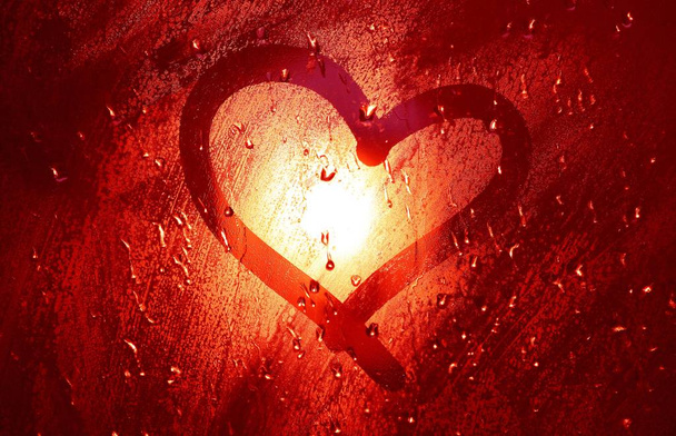 Corazón en la ventana. Pintado con un dedo sobre vidrio nebulizado durante la lluvia. Brillante bokeh de una lámpara de calle
. - Foto, Imagen