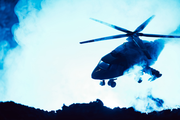Battle scene with toy helicopter above battleground with smoke on blue background  - Foto, imagen