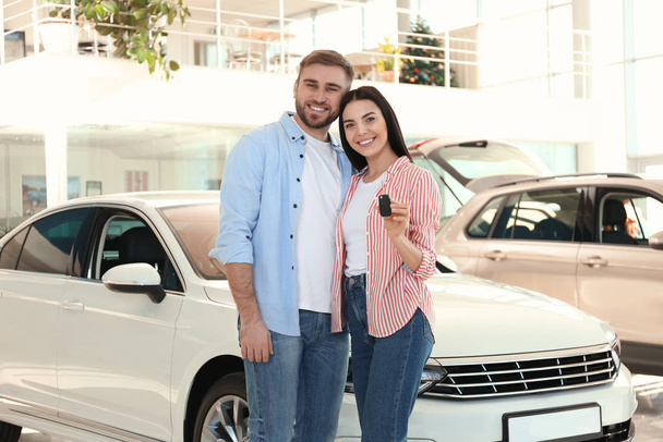 Happy couple with car key in modern auto dealership - Zdjęcie, obraz