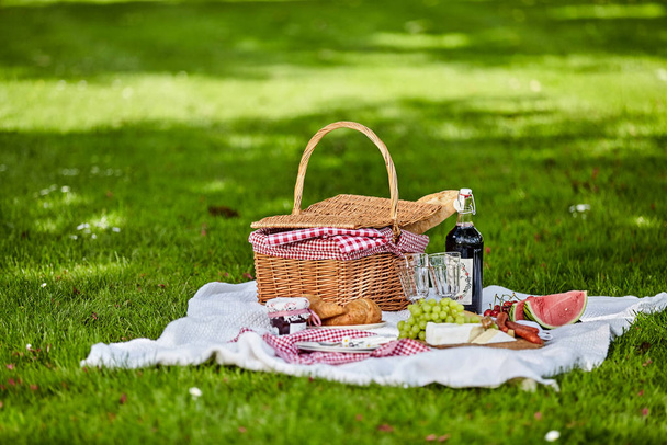 Gezond buiten zomer of lente picknick verspreid over een tapijt op een weelderig groen gazon met een fles wijn, vers fruit, kaas en brood - Foto, afbeelding