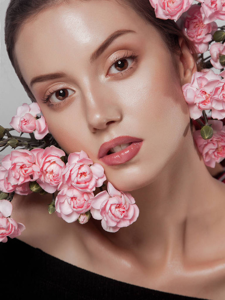 close-up beauty portrait. young beautiful woman with natural glowing makeup. pink flowers near her face. spring portrait - Photo, Image