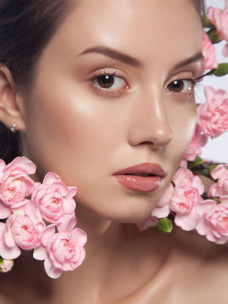 close-up beauty portrait. young beautiful woman with natural glowing makeup. pink flowers near her face. spring portrait - Photo, Image