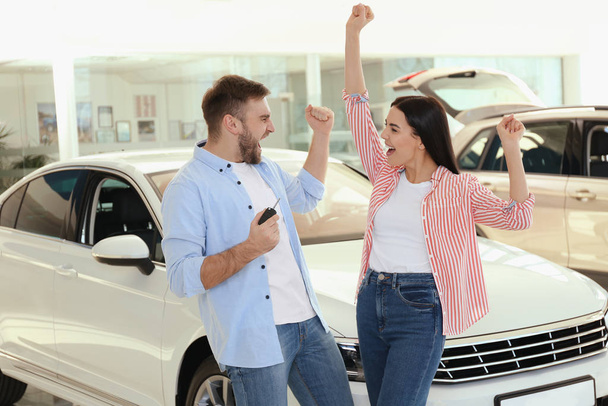 Happy couple with car key in modern auto dealership - Foto, afbeelding
