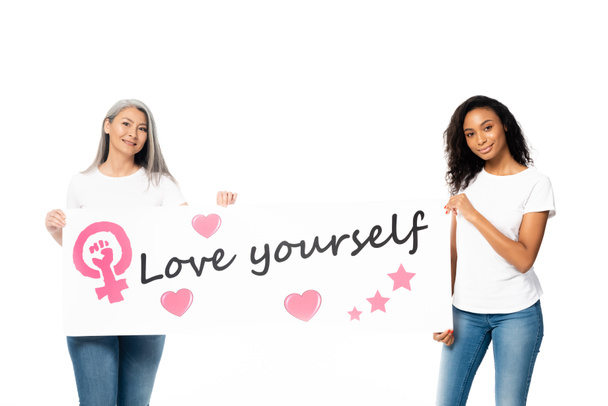 happy african american and asian women holding placard with love yourself lettering and women power sign isolated on white  - Фото, изображение