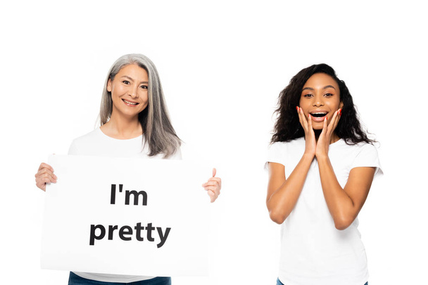 Boldog afro-amerikai és ázsiai nők közelében én vagyok szép placard elszigetelt fehér  - Fotó, kép