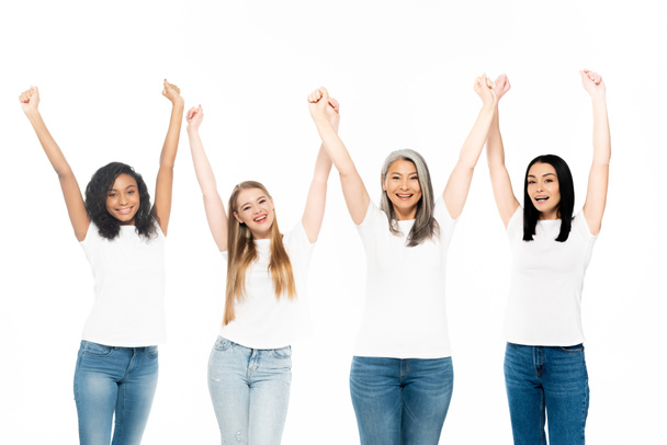 happy multicultural women in denim jeans standing with hands above head isolated on white  - Fotografie, Obrázek