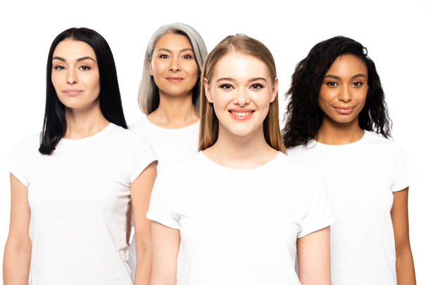 vier glückliche multikulturelle Frauen in weißen T-Shirts, die isoliert auf weiß in die Kamera schauen  - Foto, Bild