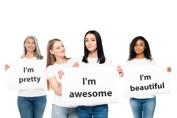 happy multicultural women in denim jeans holding posters with lettering isolated on white  - Photo, Image