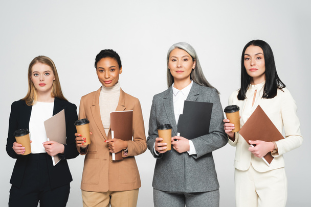 four multicultural businesswomen holding folders and paper cups isolated on white  - Photo, Image