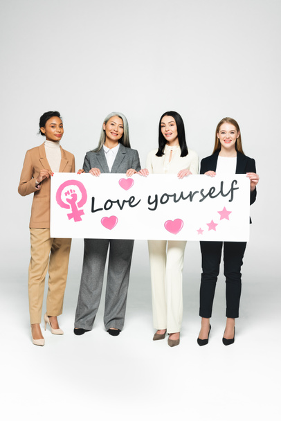 heureux multiculturelles femmes d'affaires tenant affiche avec amour vous lettrage sur blanc
  - Photo, image