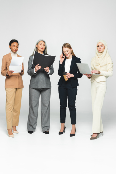 multicultural businesswomen with folders near woman talking on smartphone on white  - Photo, Image