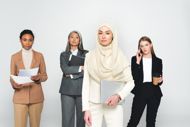 ελκυστικές πολυπολιτισμικές επιχειρηματίες κοντά στην αραβική γυναίκα με φορητό υπολογιστή απομονωμένο σε λευκό  - Φωτογραφία, εικόνα