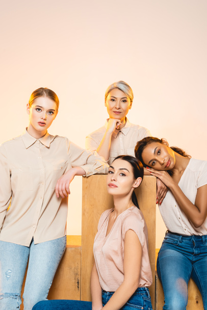 four beautiful multicultural women with makeup looking at camera isolated on beige  - Photo, Image