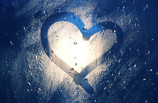 Καρδιά στο παράθυρο. Βαμμένο με ένα δάχτυλο σε θολό γυαλί κατά τη διάρκεια της βροχής. Φωτεινό bokeh από μια λάμπα του δρόμου. - Φωτογραφία, εικόνα