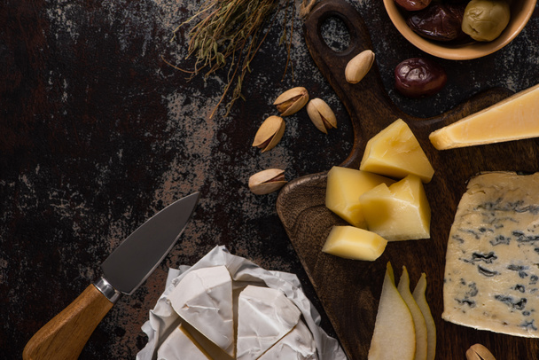 top view of cheese platter with pistachios, sliced pear, olives and knife on weathered surface - Fotoğraf, Görsel
