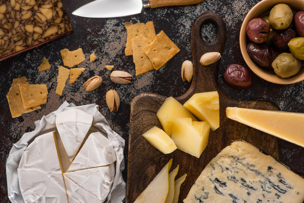 top view of cheese platter with pistachios, sliced pear, olives and crackers on weathered surface - 写真・画像
