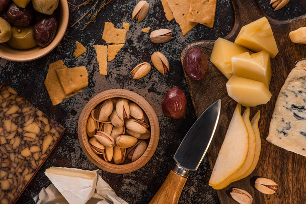 top view of cheese platter with pistachios, sliced pear, olives and crackers on weathered surface - Foto, Imagem