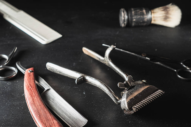 Vintage-Friseurausrüstung auf schwarzem Hintergrund. professionelle Friseurwerkzeuge. Schere, Handhaarschneider, Rasiermesser, Rasierpinsel, Kamm - Foto, Bild